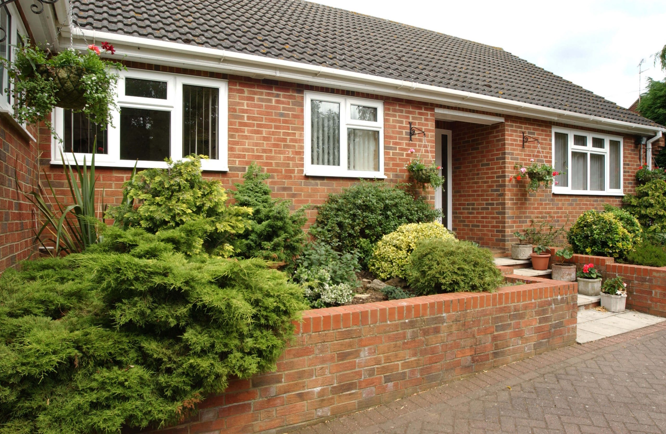 red brick bungalow with white upvc windows and a green front garden